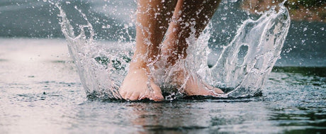 Füße in einer spritzenden Regenpfütze 